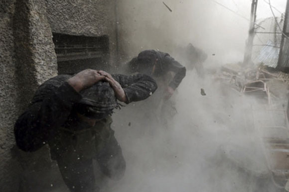 Goran Tomasevic photographs rubble falling down around fighters in Syria.